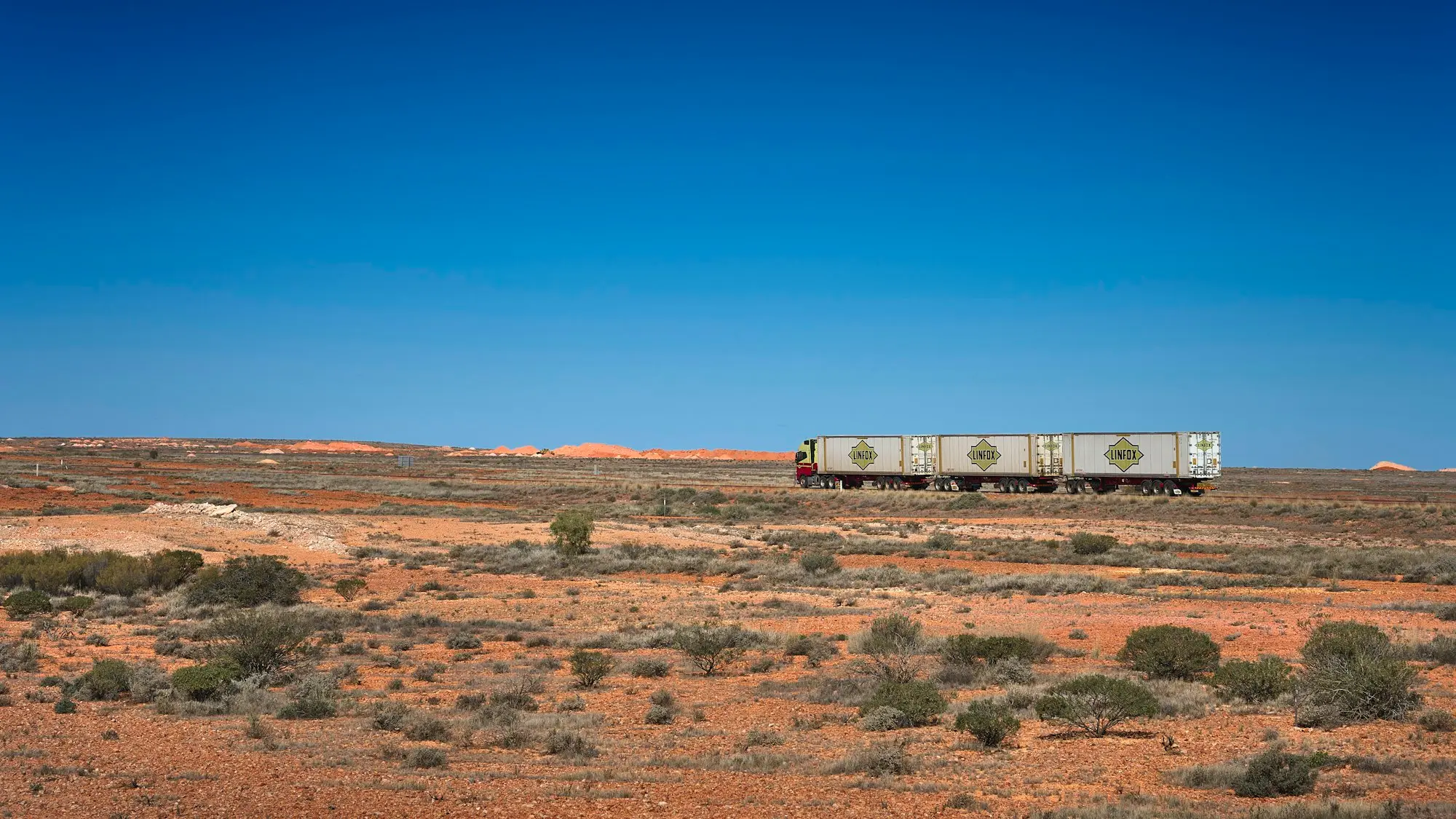 Road train travelling on the left side of the Stuart Highway through red outback country